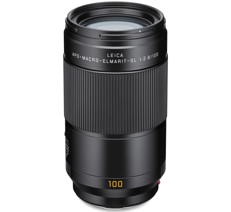 A Leica APO-Macro-Elmarit-SL 100mm f/2.8 camera lens standing upright on a white background, displaying its black cylindrical body with engraved text and yellow "100" marking near the base.