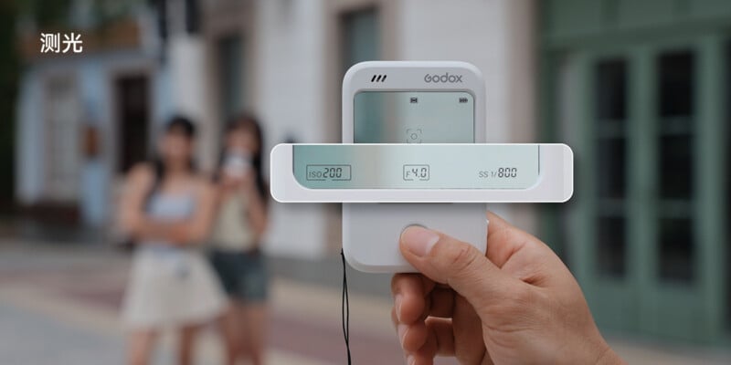 A hand holds a Godox light meter showing ISO 200, f/4.0, and shutter speed 1/800, with three people blurred in the background outdoors. Chinese text is in the upper left corner.
