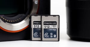 Two ProGrade 512GB CFexpress memory cards are standing upright on a white surface between a camera body and a camera lens.