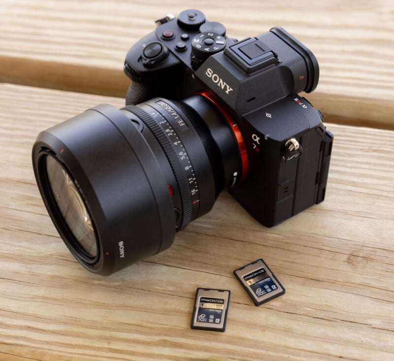 A Sony digital camera with a large lens is resting on a wooden surface next to three SD memory cards.