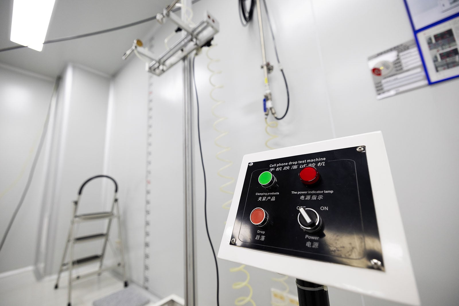 Close-up of a control panel with red and green buttons and labels in English and Chinese, in a clean, white industrial room with a metal ladder and equipment in the background.