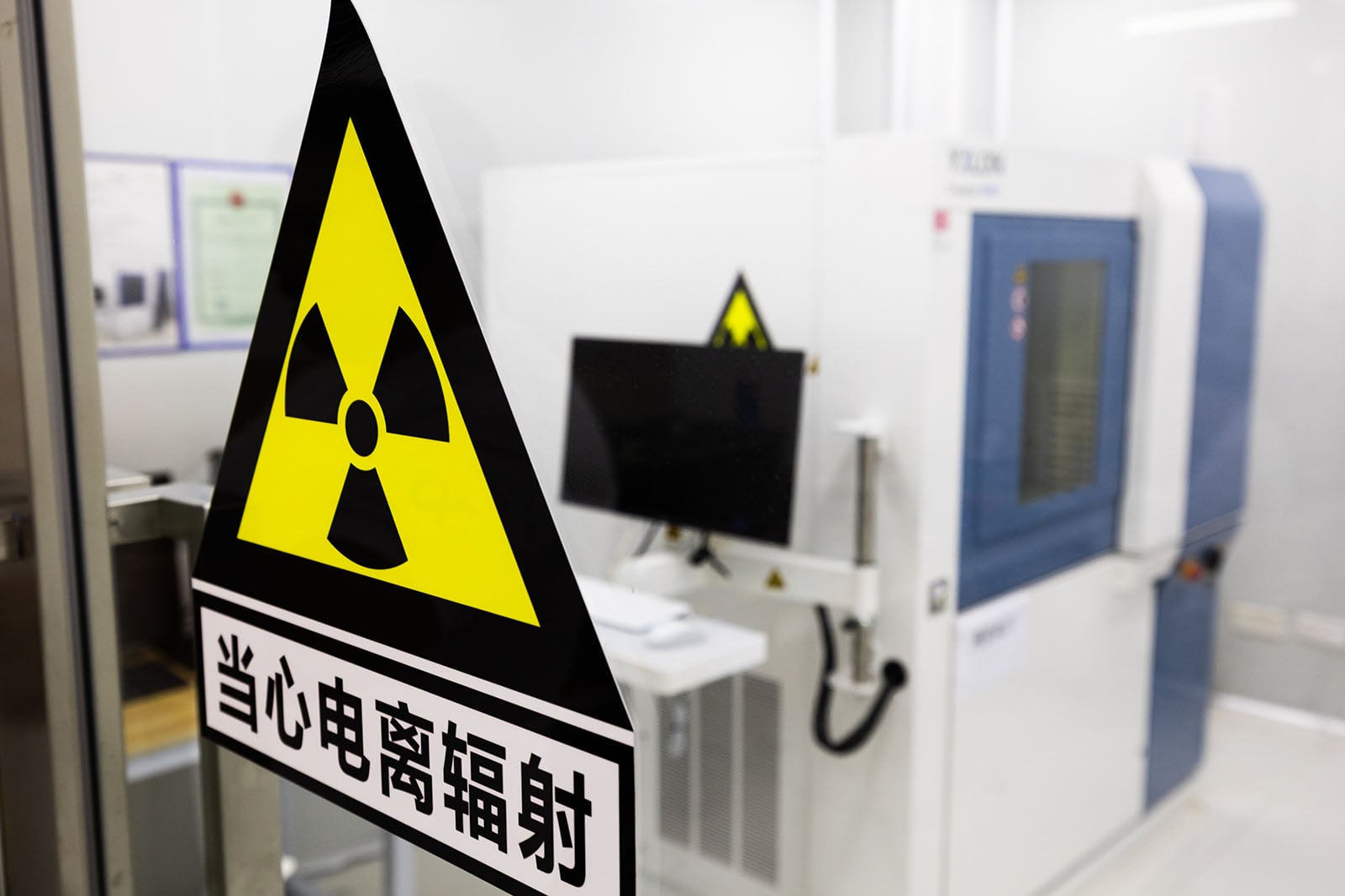 A yellow and black radiation warning sign with Chinese text is posted on a glass door in front of scientific equipment inside a laboratory or medical facility.