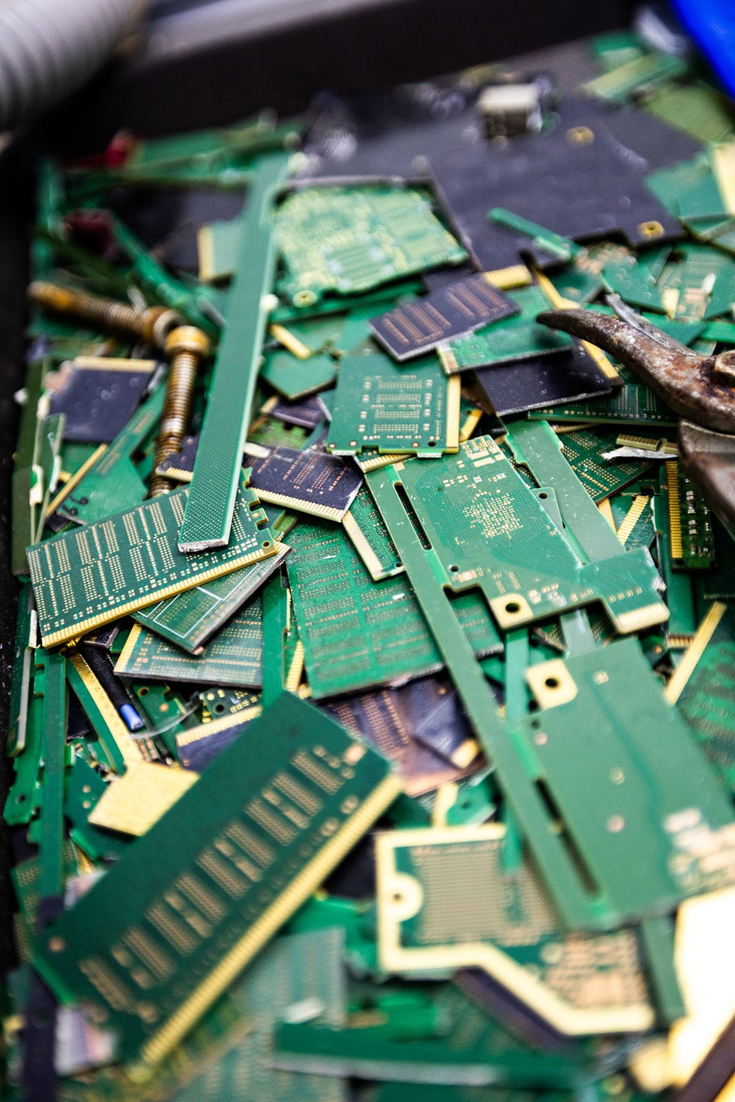 A close-up view of a pile of discarded green printed circuit boards and electronic components, including some metal parts, suggesting electronic waste or recycling.