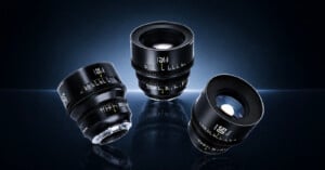 Three professional camera lenses with black bodies and white and yellow markings are displayed on a reflective surface against a dark, gradient background.