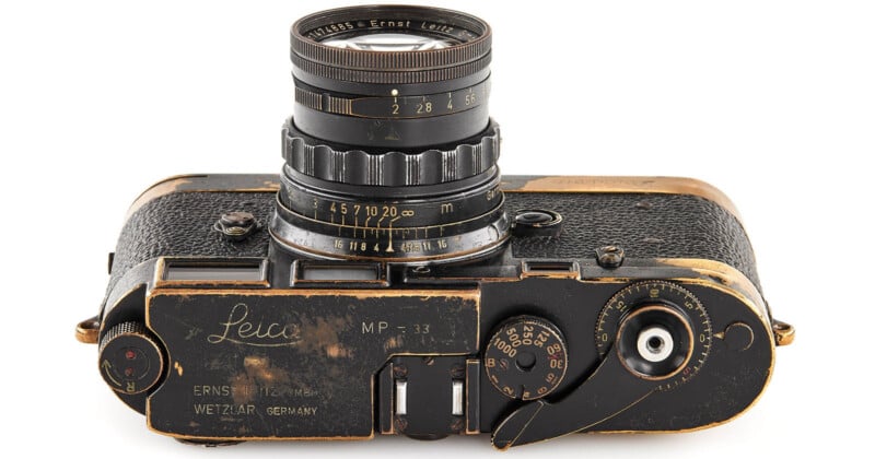 A vintage black Leica camera with visible metal wear, textured leather body, manual dials, and an attached lens marked with distance and aperture numbers.