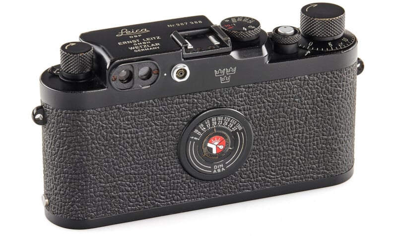 A vintage Leica camera with a textured black body, various dials and knobs on top, and a circular exposure meter on the back labeled with DIN and ASA settings.