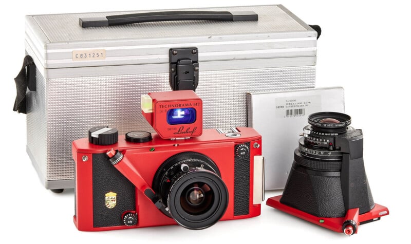 A red Linhof Technorama 617 panoramic film camera with attached lens sits in front of its silver carrying case; an additional lens is placed to the right of the camera.