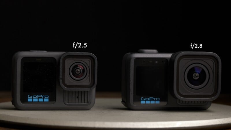 Two GoPro cameras are placed side by side on a round surface. The camera on the left has an f/2.5 lens, while the one on the right has an f/2.8 lens. Both have the GoPro logo on the front. The background is black.