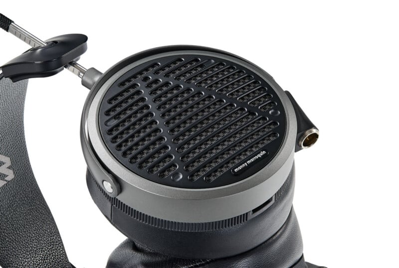 Close-up of a high-end over-ear headphone ear cup with a black metal grille, textured padding, and a visible audio jack port on the side.