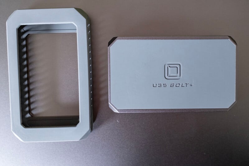 A gray plastic rectangular frame and a matching gray cover labeled "U35 BOLT+" with a square logo, both placed on a flat, dark surface.