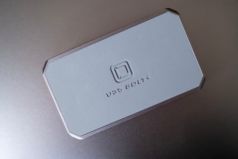 A rectangular, gray external hard drive labeled "USB BOLT+" with a square logo above the text, placed on a dark surface.