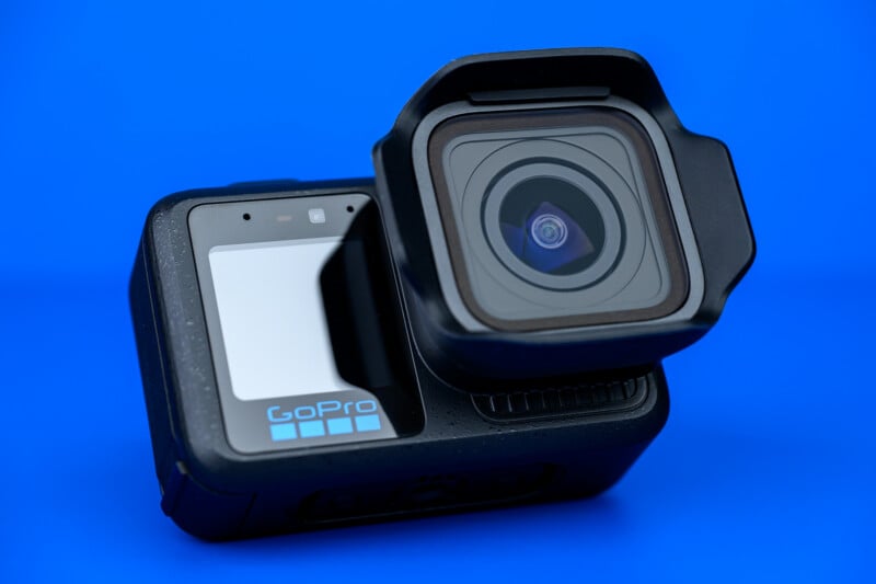 A close-up of a GoPro action camera with a protective lens cover, set against a solid bright blue background.