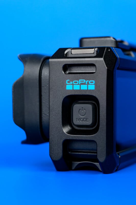 Close-up of a black GoPro camera against a bright blue background, showing the power/mode button and part of the lens housing.