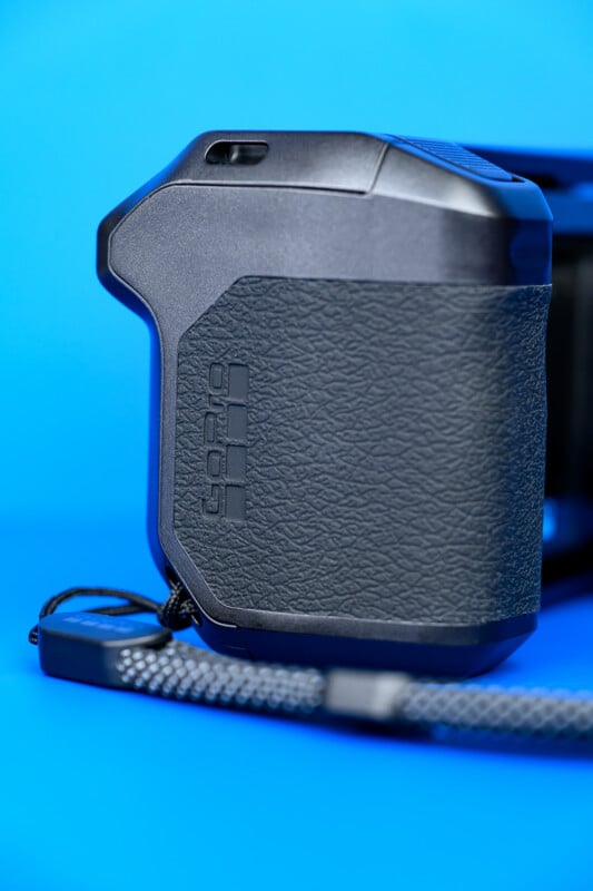 Close-up of a black GoPro camera grip with a textured surface and a wrist strap, set against a bright blue background.