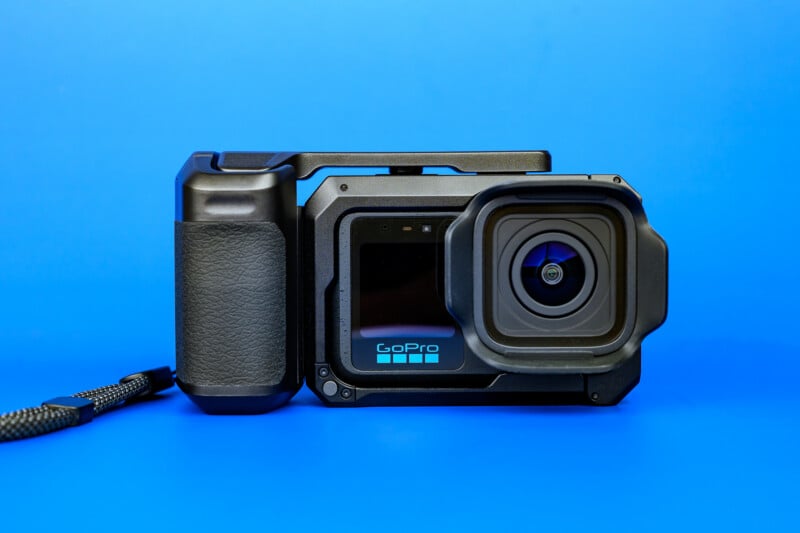 Close-up of a GoPro action camera in a protective case with a grip handle and wrist strap, set against a solid blue background.
