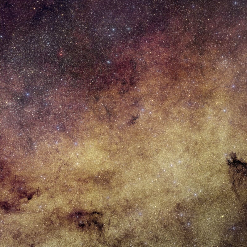 La densa región de la Vía Láctea contiene innumerables estrellas, nubes de polvo interestelar y manchas de distintos tonos de amarillo, marrón y negro en la imagen, lo que le da al universo una apariencia texturizada.