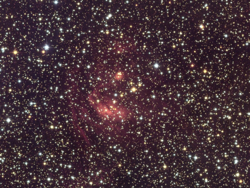 Una densa franja de estrellas esparcidas por el cielo oscuro, con algunas áreas mostrando tenues nubes rojas de gas y polvo que probablemente sean parte de una nebulosa. La escena es luminosa, con innumerables estrellas blancas y amarillas.