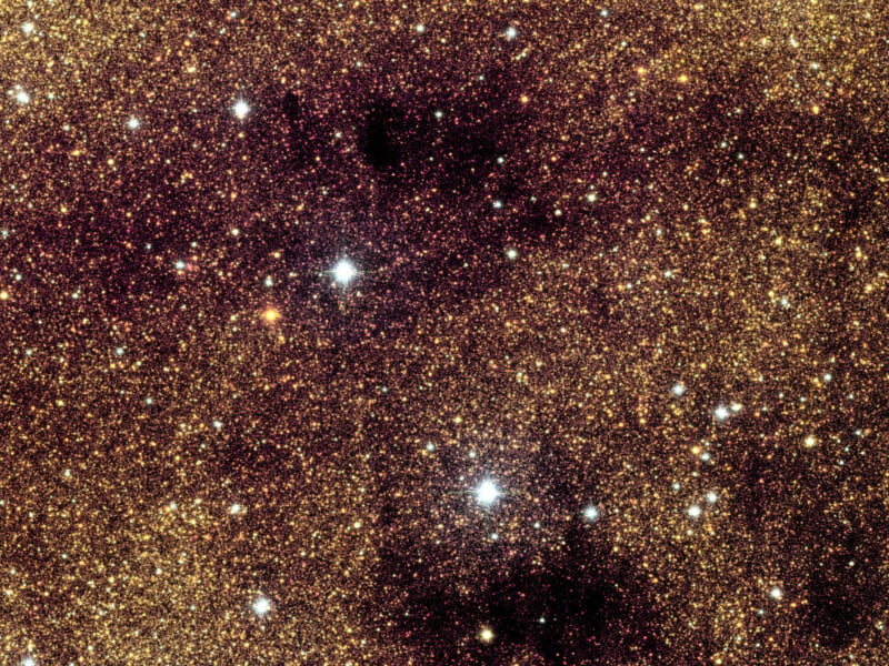 Una densa franja de estrellas amarillas y blancas brilla intensamente contra el fondo oscuro del espacio profundo, con algunas manchas oscuras oscurecidas por el polvo interestelar.