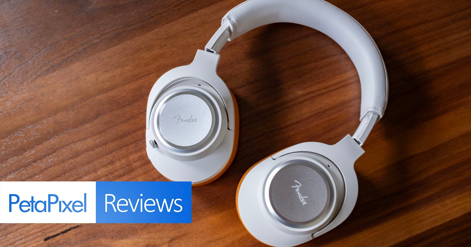 A pair of silver and white over-ear Fender headphones rest on a wooden surface. In the bottom left corner, the PetaPixel Reviews logo is visible.