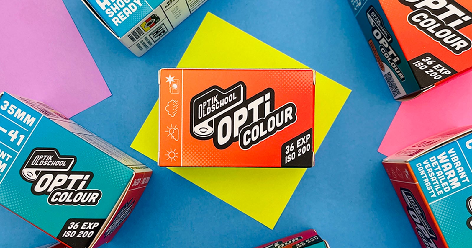 A box of Opti Colour 35mm film sits on a yellow paper, surrounded by other colorful Opti Colour film boxes on a blue background. The central box shows icons for weather conditions and "36 EXP ISO 200.