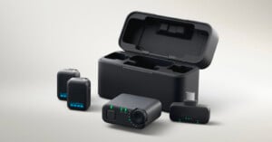 A GoPro wireless microphone system with two microphones, a receiver, a charging case, and a USB-C adapter, all shown on a light background. Green indicator lights are visible on the receiver and microphones.