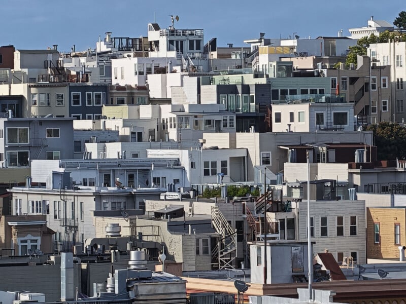 A densely packed cluster of multi-story residential buildings with flat roofs and varied facades, seen under bright daylight with blue sky in the background.
