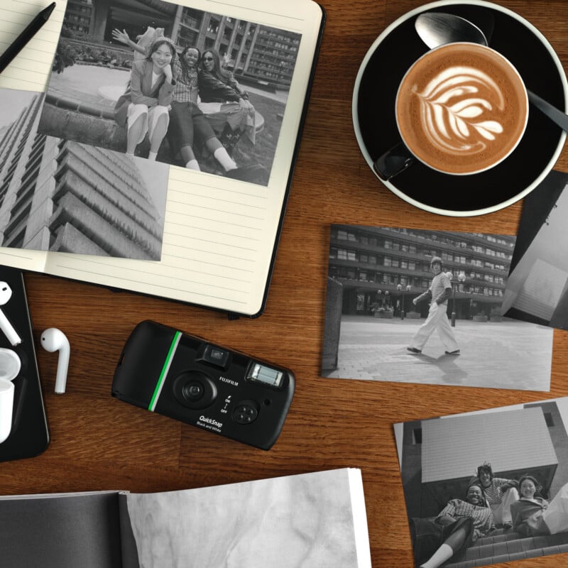 A wooden table with black-and-white photos, an instant camera, a notebook, earbuds, and a cup of latte art coffee. Some photos show people posing together and walking in an urban setting.