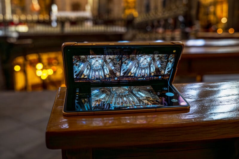 A foldable smartphone sits open on a wooden surface, displaying a detailed photo of an ornate, vaulted church ceiling, with the actual church interior blurred in the background.