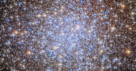 A dense cluster of bright blue, white, and orange stars against a dark background, resembling a sparkling, glowing patch in space. This image shows a globular star cluster with many stars close together.