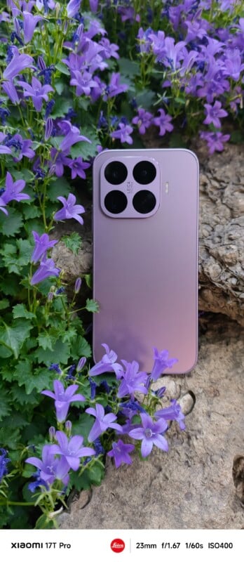 A lavender Xiaomi 17T Pro smartphone rests on a rock surrounded by blooming purple flowers and green leaves. Photography details are displayed at the bottom of the image.
