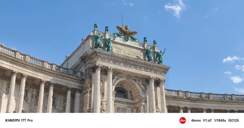 A grand historic building with ornate columns, green statues, and a golden eagle on the roof, set against a blue sky with a few clouds. Photo details are overlaid at the bottom.