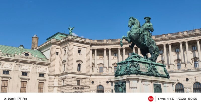 A bronze equestrian statue stands in front of a grand, historic building with columns and a green roof under a clear blue sky.