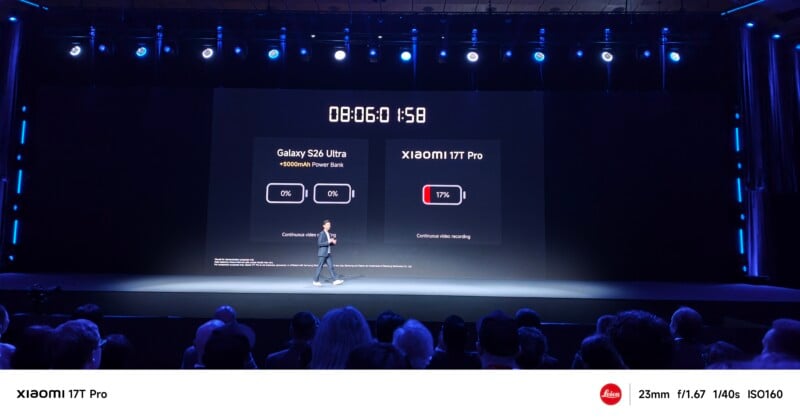 A presenter stands on stage in front of a large screen comparing the Galaxy S24 Ultra and Xiaomi 14T Pro battery performance, with a timer showing 8 hours and 6 minutes and a large audience watching.