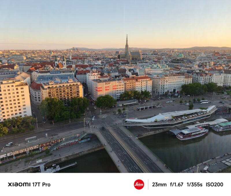 Aerial view of a city with a river, bridges, boats, and historic buildings. St. Stephen’s Cathedral stands out in the center. The image is bright and clear, taken at sunset with urban streets and greenery visible.