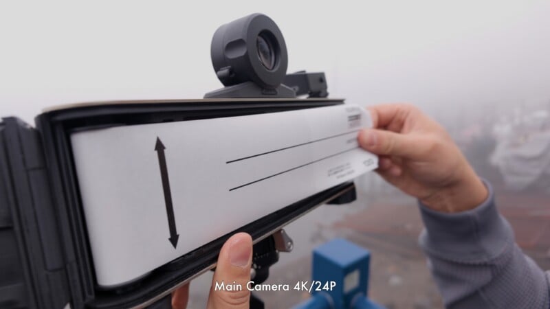 A person holds a calibration chart against a camera in an outdoor, foggy environment. The chart has arrows and lines, and "Main Camera 4K/24P" text appears at the bottom of the image.