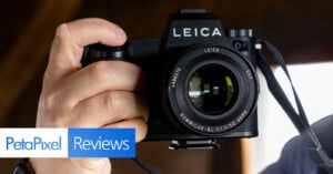 A person holds a Leica camera close to their face, with the lens facing the viewer. The image has "PetaPixel Reviews" text in the lower left corner.