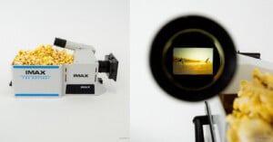 A box shaped like an IMAX film camera, filled with popcorn, sits against a white background. The camera’s viewfinder shows a desert scene from a movie.