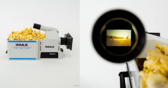 A box shaped like an IMAX film camera, filled with popcorn, sits against a white background. The camera’s viewfinder shows a desert scene from a movie.