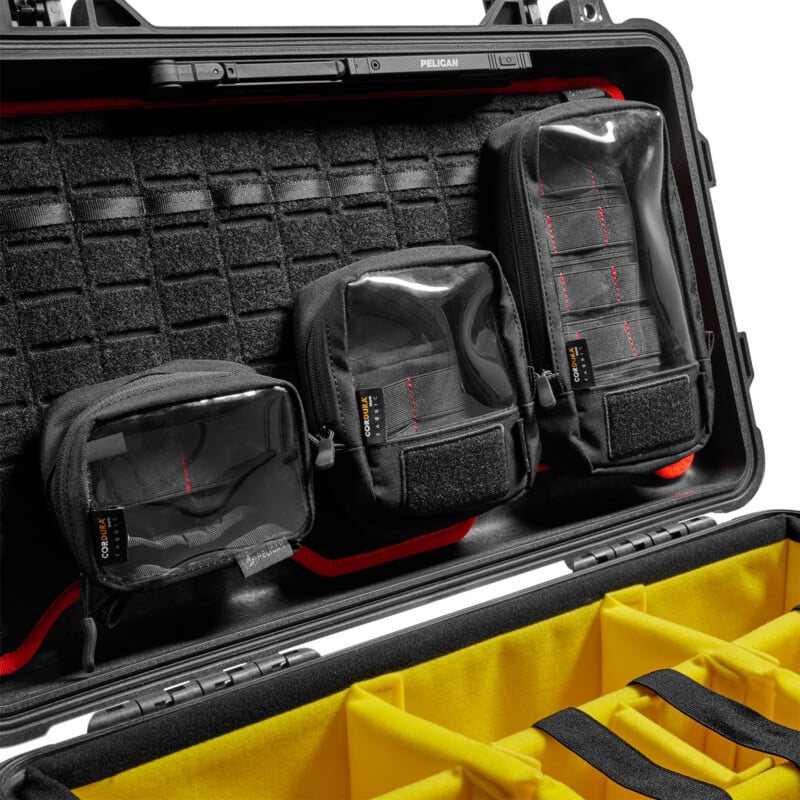A hard-shell black case with a yellow interior holds three black zippered pouches with clear fronts and red stitching, attached to the lid, and yellow dividers in the main compartment.