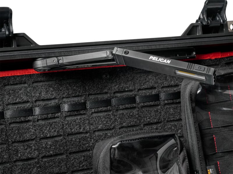 A close-up of an open black hard case with a mounted Pelican-branded foldable LED light attached to the lid, revealing padded and organized interior compartments.