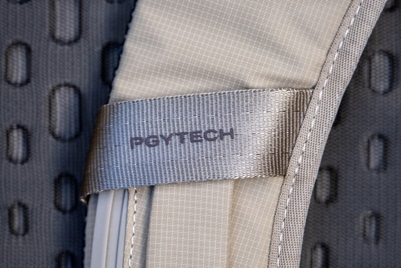 Close-up of a gray strap with the brand name "PGYTECH" printed on it, attached to a padded fabric surface with a textured, dotted pattern in the background.