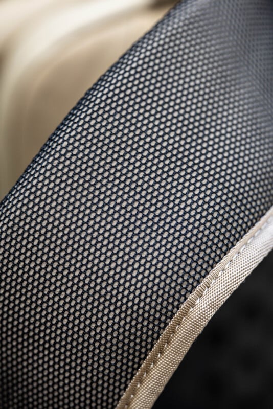 Close-up of a curved, padded surface covered in tightly woven black and beige mesh fabric, showing a hexagonal pattern and beige trim along the edge.
