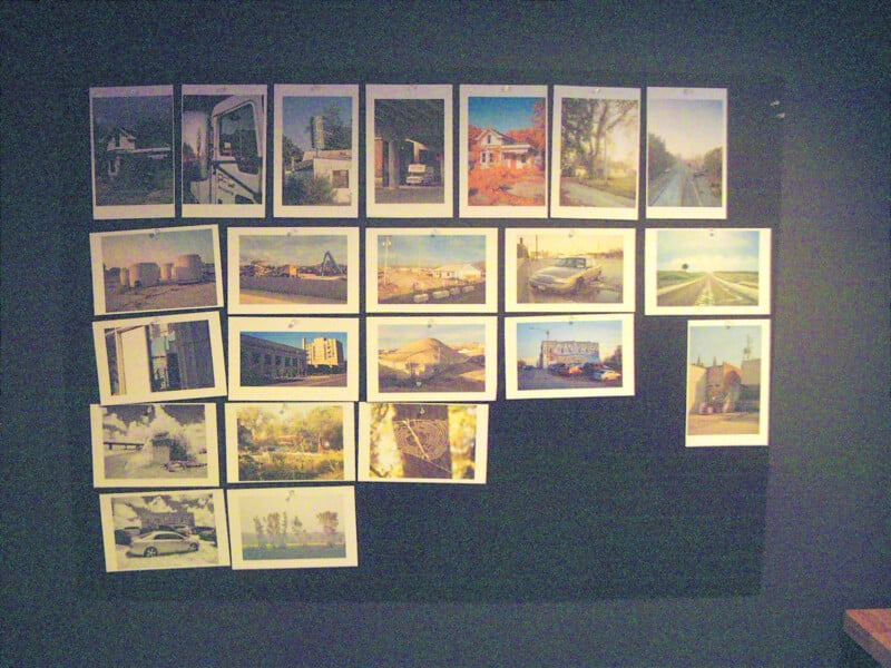 A display of several photographs arranged in rows on a dark wall, featuring images of houses, buildings, streets, cars, and outdoor scenes in various lighting conditions.