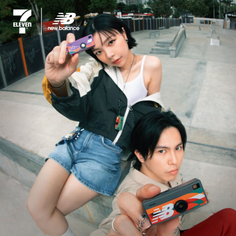 A young woman and man pose playfully at a skate park, each holding up a card and camera with colorful New Balance branding. Logos for 7-Eleven and New Balance appear in the upper left corner.