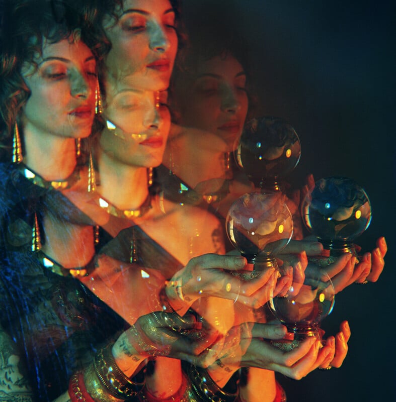 A woman with curly hair and gold jewelry is shown in a colorful, blurred multiple exposure effect, holding two glass spheres in her hands, creating a mystical, surreal atmosphere.