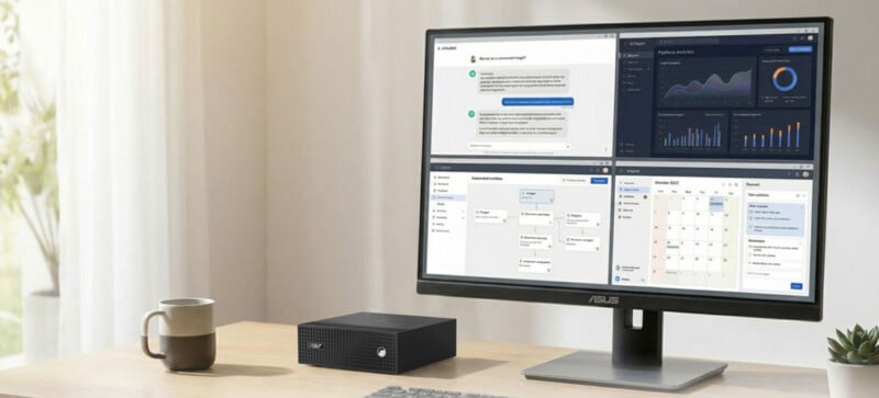 A desktop computer with a large monitor displays charts, graphs, and messaging on a tidy desk with a keyboard, mouse, coffee mug, small computer tower, and natural light from a nearby window.
