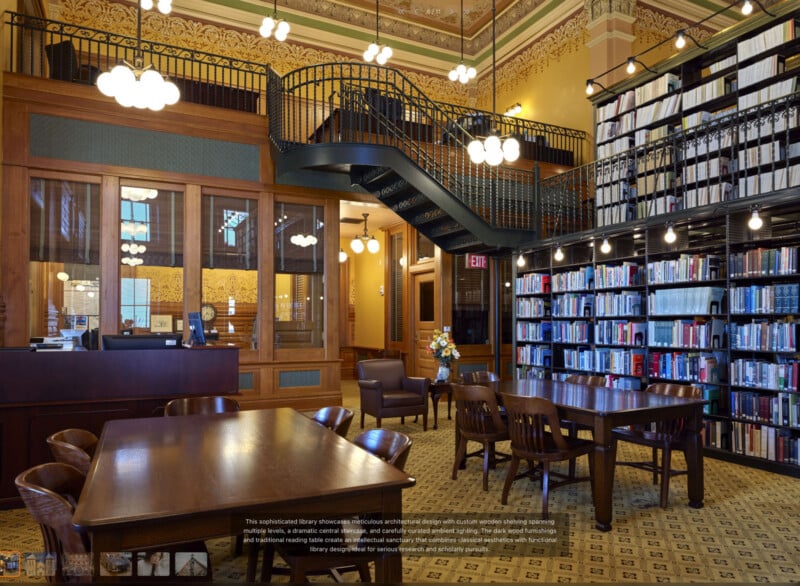 A spacious, elegant library room with tall bookshelves, wooden tables and chairs, a decorative staircase, ornate ceiling, and large pendant lights, creating a warm, inviting atmosphere for reading and study.