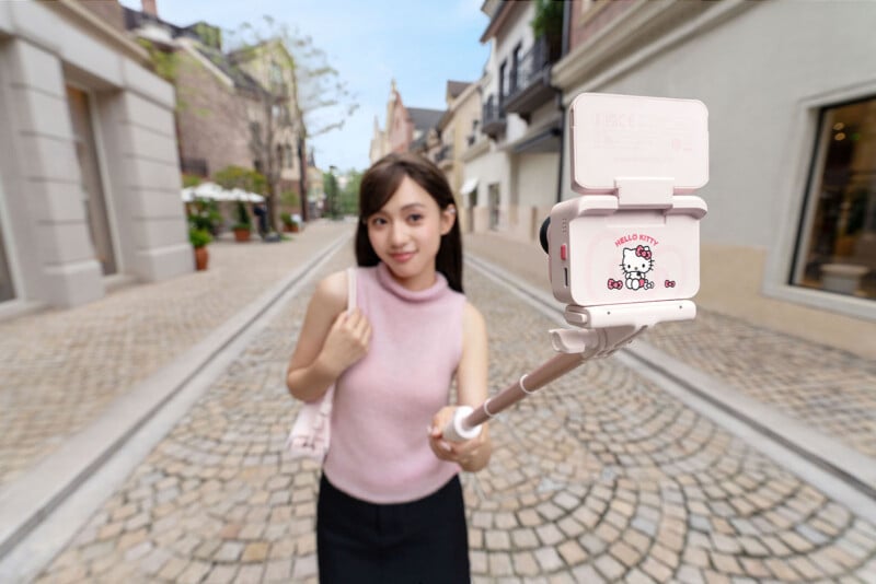 A young woman holding a pink Hello Kitty selfie stick outdoors.