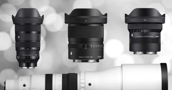 Three black camera lenses with lens hoods are displayed upright against a blurred gray background, next to a large white telephoto lens positioned horizontally at the bottom of the image.