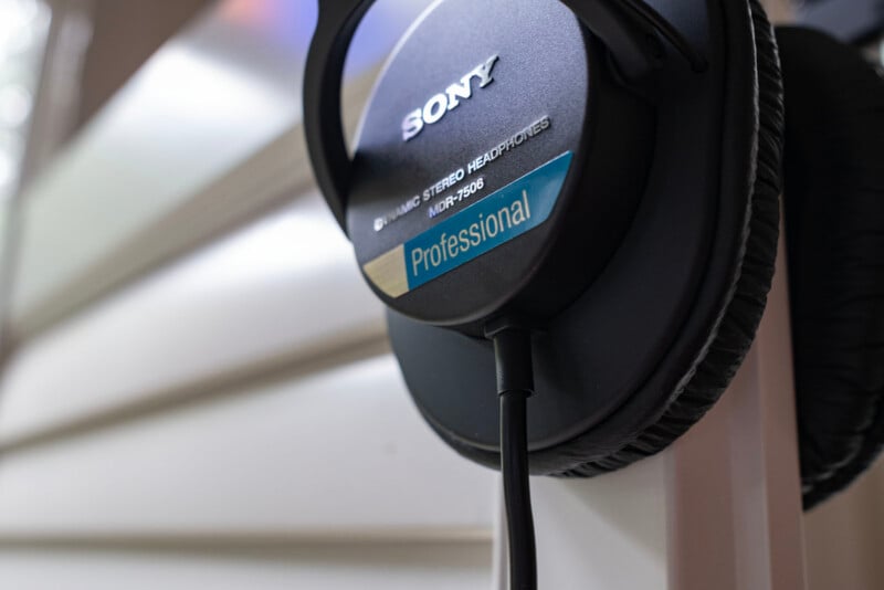 Close-up of a pair of black Sony MDR-7506 Professional Dynamic Stereo Headphones hanging on a white surface with a blurred background.